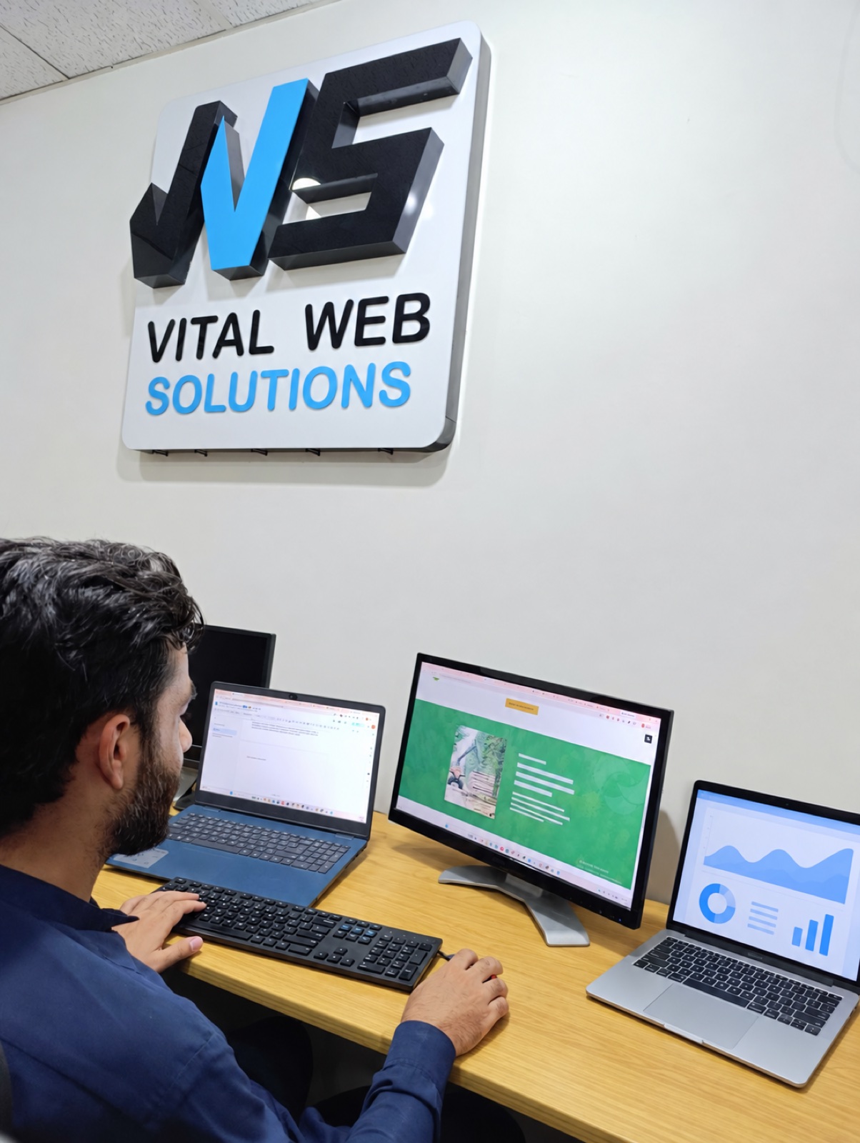 Vital Web Solution team member working at a tidy desk beneath the original office sign